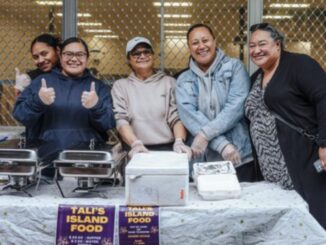 Five women smiling behind a food stall with trays of island food at a Pacific Night Market in Cannons Creek.